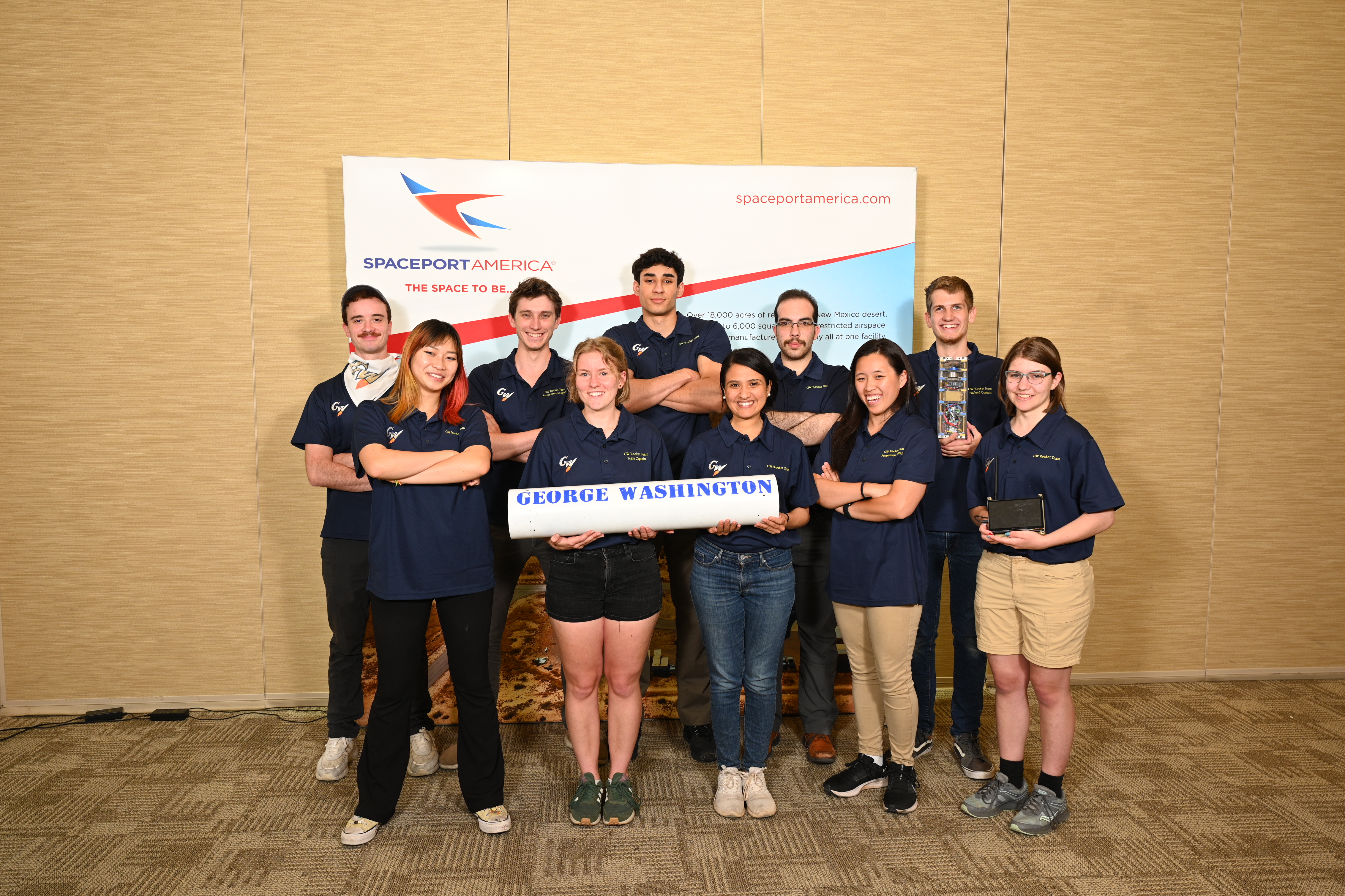 GW Rocket Team smiling in front of Spaceport America banner