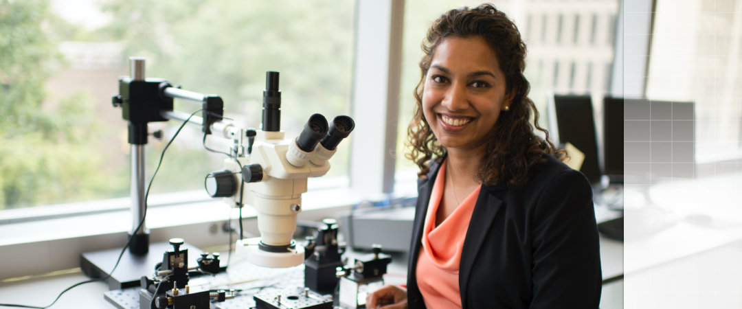 Professor smiling, sitting in front of a microscope