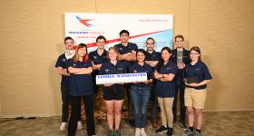 GW Rocket Team smiling in front of Spaceport America banner